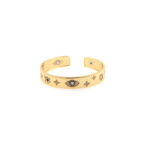 May include: Gold cuff bracelet with a decorative design of blue and white evil eyes and stars. The bracelet is made of metal and has a polished finish.