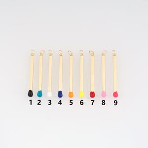 Puede incluir: Nueve colgantes dorados con forma de cerilla y puntas de colores. Las puntas son negras, turquesas, blancas, azules, naranjas, amarillas, rojas, rosas y fucsias. Cada colgante tiene un pequeño lazo en la parte superior.