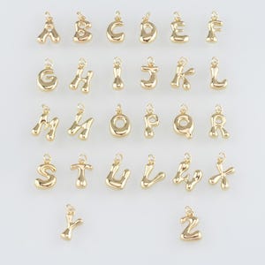 Può includere: Un set di 26 ciondoli in metallo dorato a forma di lettere dell'alfabeto. Ogni lettera è in un carattere unico, leggermente ondulato. I ciondoli sono perfetti per aggiungere un tocco personale ai gioielli.