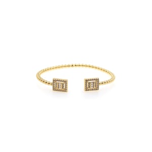 May include: A gold bangle bracelet with two square-shaped charms. Each charm is adorned with small clear stones.