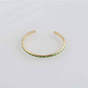 Puede incluir: Un brazalete de puño dorado con un diseño de esmalte verde. El brazalete tiene un diseño abierto y se muestra sobre un fondo blanco. El esmalte verde es una serie de pequeños puntos espaciados uniformemente alrededor del brazalete.