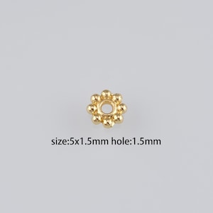 Puede incluir: Cuentas de metal de color dorado con un agujero redondo en el centro. La cuenta tiene un diámetro de 5 mm y un agujero de 1,5 mm. La cuenta está rodeada de cuentas más pequeñas.