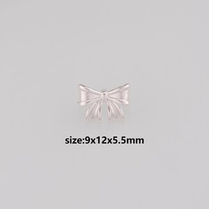 May include: A small, silver-colored bow-shaped charm. The charm is approximately 0.35 inches long, 0.47 inches wide, and 0.22 inches thick. The text "size:9x12x5.5mm" is below the charm. The charm is on a light gray background.
