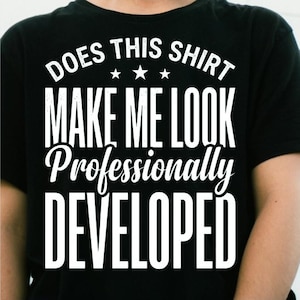 Peut inclure: Un t-shirt noir avec un texte blanc qui indique DOES THIS SHIRT MAKE ME LOOK Professionally DEVELOPED avec trois petites étoiles centrées entre la première et la deuxième ligne de texte. Le motif est imprimé dans une police grasse.
