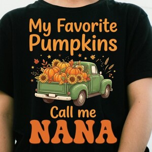 May include: A black t-shirt featuring a graphic of a green vintage pickup truck loaded with orange pumpkins and sunflowers. The text above the truck reads My Favorite Pumpkins and the text below the truck reads Call me NANA in orange letters.