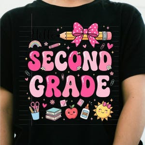 Peut inclure: Un t-shirt noir avec un motif graphique portant l'inscription "Hello SECOND GRADE" en lettres roses. Le design comprend un crayon jaune avec un nœud rose à pois, un arc-en-ciel, des livres, une pomme rouge, de la colle et un soleil souriant.