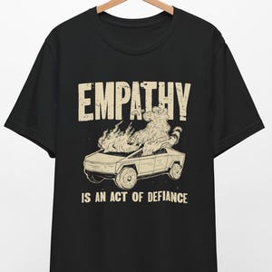 May include: Black t-shirt with a graphic of a car on fire and the text "EMPATHY IS AN ACT OF DEFIANCE".