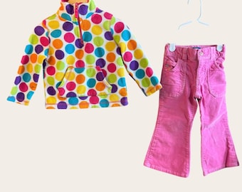Puede incluir: Un suéter de forro polar de manga larga con un patrón de lunares multicolor, cuello con cremallera de un cuarto y bolsillo frontal, junto con pantalones de pana rosa liso con cierre de botón y bolsillos delanteros.