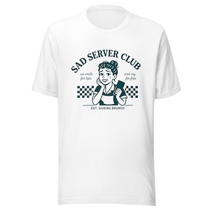 Może przedstawiać: Biała koszulka z turkusową grafiką. Grafika głosi "SAD SERVER CLUB" z ilustracją płaczącej kelnerki i tekstem "we smile for tips and cry for free. EST. DURING BRUNCH."