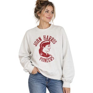Peut inclure: Un sweat-shirt à col rond gris clair avec une impression graphique bordeaux sur la poitrine. Le motif présente une illustration de profil d'une personne avec une coupe mulet, entourée du texte John Harris Pioneers en police serif.