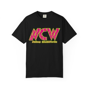 May include: Black t-shirt featuring a neon pink and green graphic of the letters "NCW" in a distressed style. The text "Nukem ClothWorks" is below the graphic in green. The t-shirt has a crew neck.