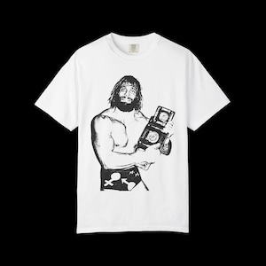 Puede incluir: Camiseta blanca con una ilustración en blanco y negro de un luchador sosteniendo un cinturón de campeonato. El gráfico representa una figura musculosa con pelo largo y barba. La camiseta tiene cuello redondo y mangas cortas.