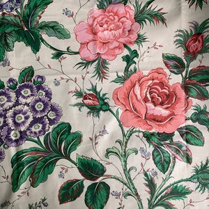 May include: A white fabric with a floral pattern featuring pink and red roses, purple flowers, and green leaves.
