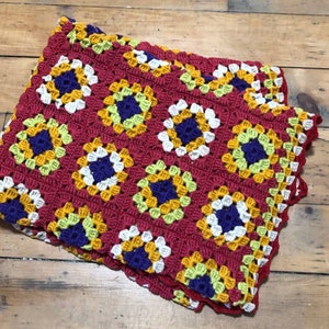 May include: A crocheted blanket with a granny square pattern in shades of red, white, yellow, green, and purple.