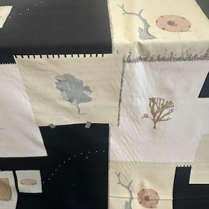 May include: A fabric quilt featuring a patchwork design of alternating black and cream-colored squares. The cream squares display botanical and marine illustrations, including coral, seaweed, and sand dollars, with visible stitched edges.