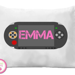 May include: White pillow with a black video game controller design. The controller has a screen with the name "EMMA" in pink letters. The pillow has a pink and white logo in the bottom left corner.