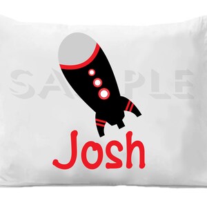 Op de afbeelding: Wit kussenovertrek met een zwart en rode raket afbeelding en de naam "Josh" in rode letters.