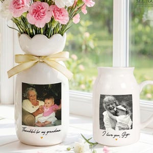 May include: A white ceramic vase with a scalloped rim and a cream ribbon, featuring a black and white photo of an older person and a child with the text "Thankful for my grandma," next to a white mug with a photo of the same pair and "I love you, Gigi."