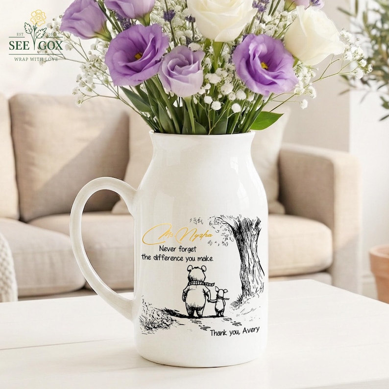 May include: White ceramic vase with a handle, filled with purple and white flowers. The vase features a black and gold illustration of a bear and a smaller animal, with the text "Never forget the difference you make". The vase has the text "Thank you, Avery".
