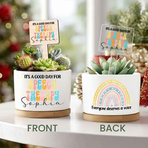 May include: Two white ceramic planters with succulents. The front planter has the text "It's a good day for speech therapy Sophia" and a wooden sign with the same text. The back planter has a rainbow design and the text "Everyone deserves a voice."
