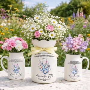 May include: Three white ceramic vessels featuring a floral stethoscope graphic and the text: Never underestimate the difference you have made, and the lives you have touched. Amanda, RN. Happy Retirement 2026. The vessels contain bouquets of flowers.
