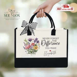 May include: A black and white tote bag with black handles and a striped bow. The bag features a floral design and the text "NEVER FORGET THE Difference YOU MAKE Elizabeth".
