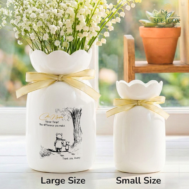 May include: Two white ceramic vases with scalloped rims and gold ribbon accents. The larger vase features a Winnie the Pooh illustration with text that reads "Never forget the difference you make. Thank you, Avery." The vases are labeled "Large Size" and "Small Size".