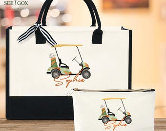 May include: A white tote bag and matching cosmetic bag with a black base and handles. Both bags feature a golf cart design with the name "Sophia" in an orange script. The tote bag has a black and white striped ribbon tied to the handle.