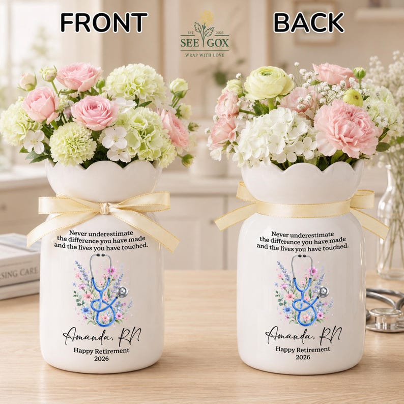 May include: A white ceramic vase with a scalloped rim and a beige ribbon, filled with pink and white flowers. The vase features a blue stethoscope graphic, floral accents, and the text: Never underestimate the difference you have made and the lives you have touched. Amanda, RN. Happy Retirement 2026.