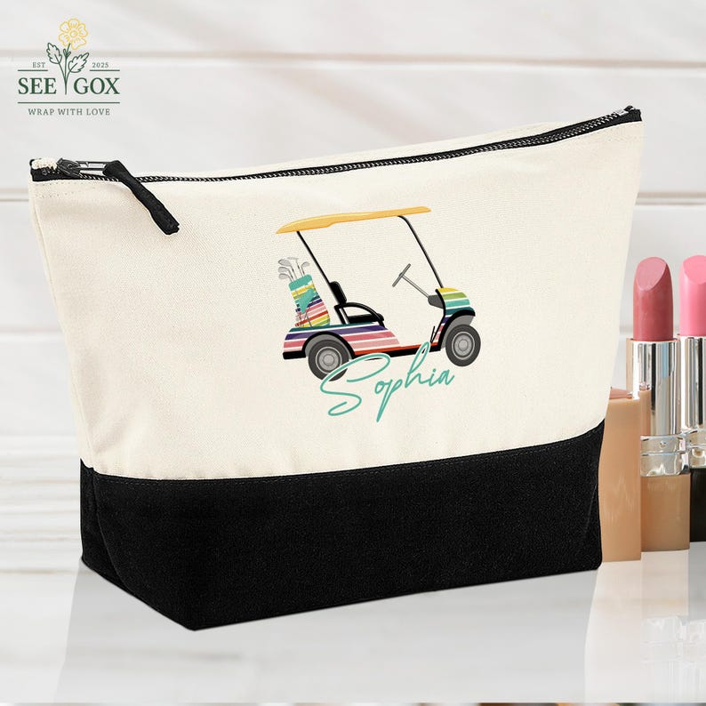 Puede incluir: Bolsa de cosm&eacute;ticos de lona con base y cremallera negras. La bolsa presenta un gr&aacute;fico de carrito de golf colorido con el nombre "Sophia" en escritura turquesa. La parte superior es de color crema.