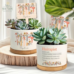 May include: Two white ceramic planters with succulents, featuring a floral design with hair styling tools and the name "Sophia." One planter has a wooden sign, the other a clear sign. The text "Hairapist" is on one planter.