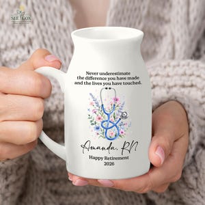 May include: A white ceramic mug featuring a blue stethoscope illustration surrounded by pink and purple flowers. The text reads: Never underestimate the difference you have made and the lives you have touched. Amanda, RN, Happy Retirement 2026.