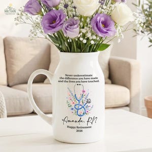 May include: A white ceramic pitcher vase featuring a blue stethoscope graphic surrounded by colorful flowers. The text reads: Never underestimate the difference you have made and the lives you have touched. Amanda, RN. Happy Retirement 2026.