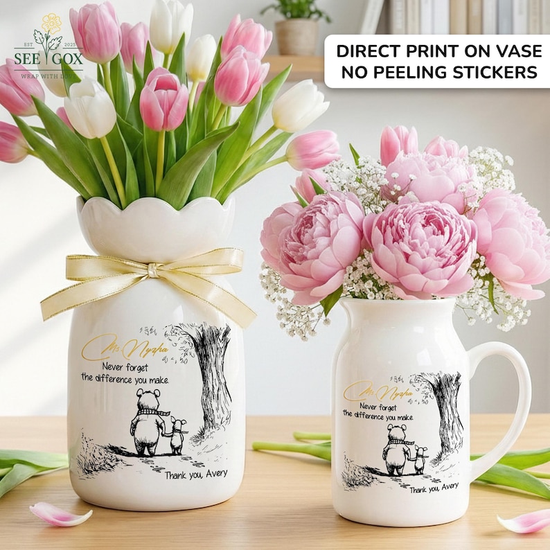 May include: Two white ceramic vases with floral arrangements. One vase holds pink and white tulips, the other holds pink peonies. Both vases have a bear and child illustration with the text "Never forget the difference you make."