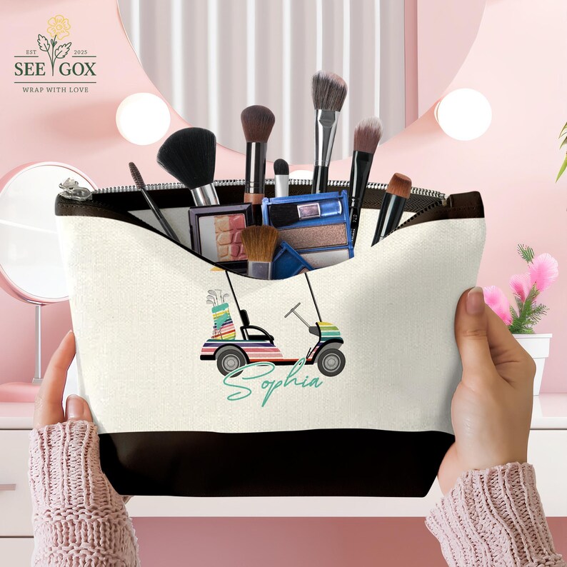 Puede incluir: Un neceser de lona con base y cremallera negras, lleno de brochas y productos de maquillaje. La bolsa presenta un dise&ntilde;o de carrito de golf colorido con el nombre "Sophia" en una fuente cursiva.