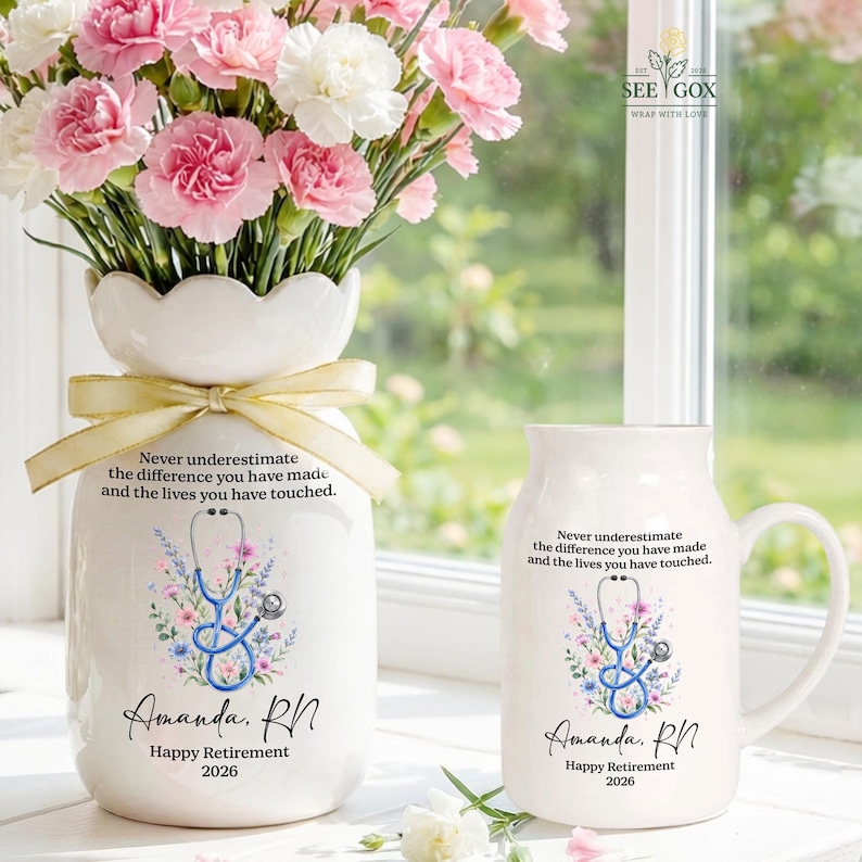 May include: A white ceramic vase with a scalloped rim and a matching white ceramic mug, both featuring a blue stethoscope graphic, floral accents, and the text "Never underestimate the difference you have made and the lives you have touched. Amanda, RN. Happy Retirement 2026."