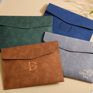 May include: Four personalized document holders in green, blue, brown, and gray. Each holder features a flap closure and embossed text: "Calvin", "Evan", "Daniel", and "Father's Day". The holders are arranged on a light-colored surface.