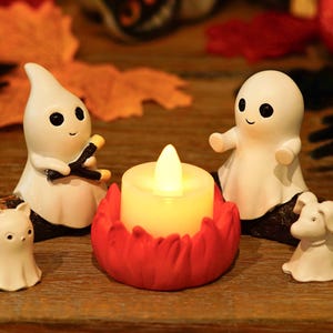 Peut inclure: Une décoration sur le thème d'Halloween avec des figurines de fantômes blancs, un petit chat et un chien, disposés autour d'une bougie lumineuse dans un support en forme de fleur rouge. Les figurines ont des yeux noirs et des visages souriants.