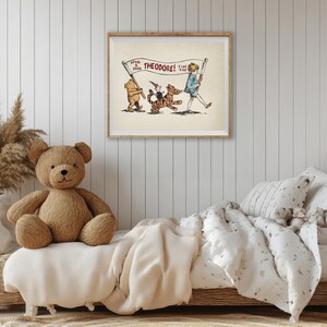 May include: A framed vintage illustration with a bear, tiger, and boy, with the text "THEODORE!". The artwork hangs above a bed with a teddy bear and neutral-toned bedding. The room has a cozy, inviting atmosphere.