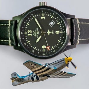 May include: A black wristwatch with a black leather band and white stitching. The watch face is black with white numerals and hands. Below the watch is a model airplane with the text "Louisiana Kid".