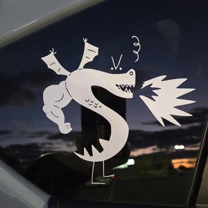 May include: White vinyl decal of a cartoon dragon on a car window. The dragon has a muscular arm, wings, and is breathing fire. The decal includes the letter "V" and a swirl above the dragon's head.