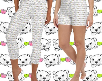 May include: White leggings and shorts with a repeating pattern of cartoon dog faces and candy hearts. The leggings are cropped at the calf, and the shorts are a short length. The background features a similar dog face pattern.