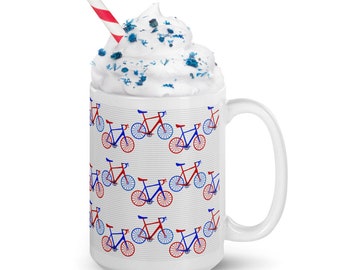 May include: White ceramic mug with a repeating pattern of red and blue bicycles. The mug has a white handle and is filled with whipped cream, blue sprinkles, and a red and white striped straw.