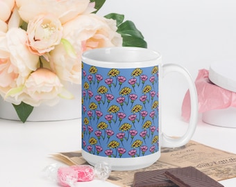 May include: A white ceramic mug with a blue background and a repeating pattern of pink and yellow flowers. The mug has a large handle.