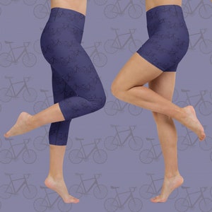 May include: Navy blue yoga leggings and shorts with a repeating bicycle pattern. The leggings are cropped at the calf, and the shorts are high-waisted. The background is a light purple color with a faded bicycle pattern.