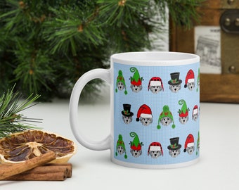 May include: White ceramic mug with a blue background and a repeating pattern of grey dogs wearing various Christmas hats, including Santa hats, elf hats, and top hats.
