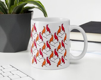 May include: White ceramic mug featuring a repeating pattern of stylized birds in shades of red and orange perched on thin black lines. The mug has a curved handle and is suitable for hot or cold beverages.
