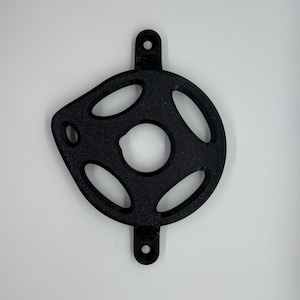 May include: Black metal bicycle chain guard with an oval design and multiple cut-out openings. The guard has two mounting holes and a central opening. The object is set against a white background.