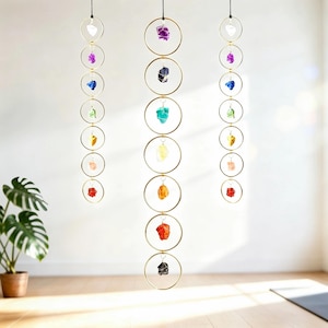 May include: Three hanging mobiles with crystals. Each mobile has gold-coloured rings, each holding a different coloured crystal. The crystals include white, purple, blue, green, yellow, orange, red, and black. The crystals are suspended from a black cord.