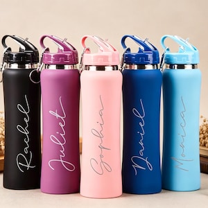 Könnte beinhalten: Fünf personalisierte Wasserflaschen in Schwarz, Lila, Rosa, Blau und Hellblau. Jede Flasche hat einen silbernen Deckel und einen Namen in Schreibschrift. Die Flaschen werden auf einem neutralen Hintergrund mit Trockenblumen und Büchern präsentiert.